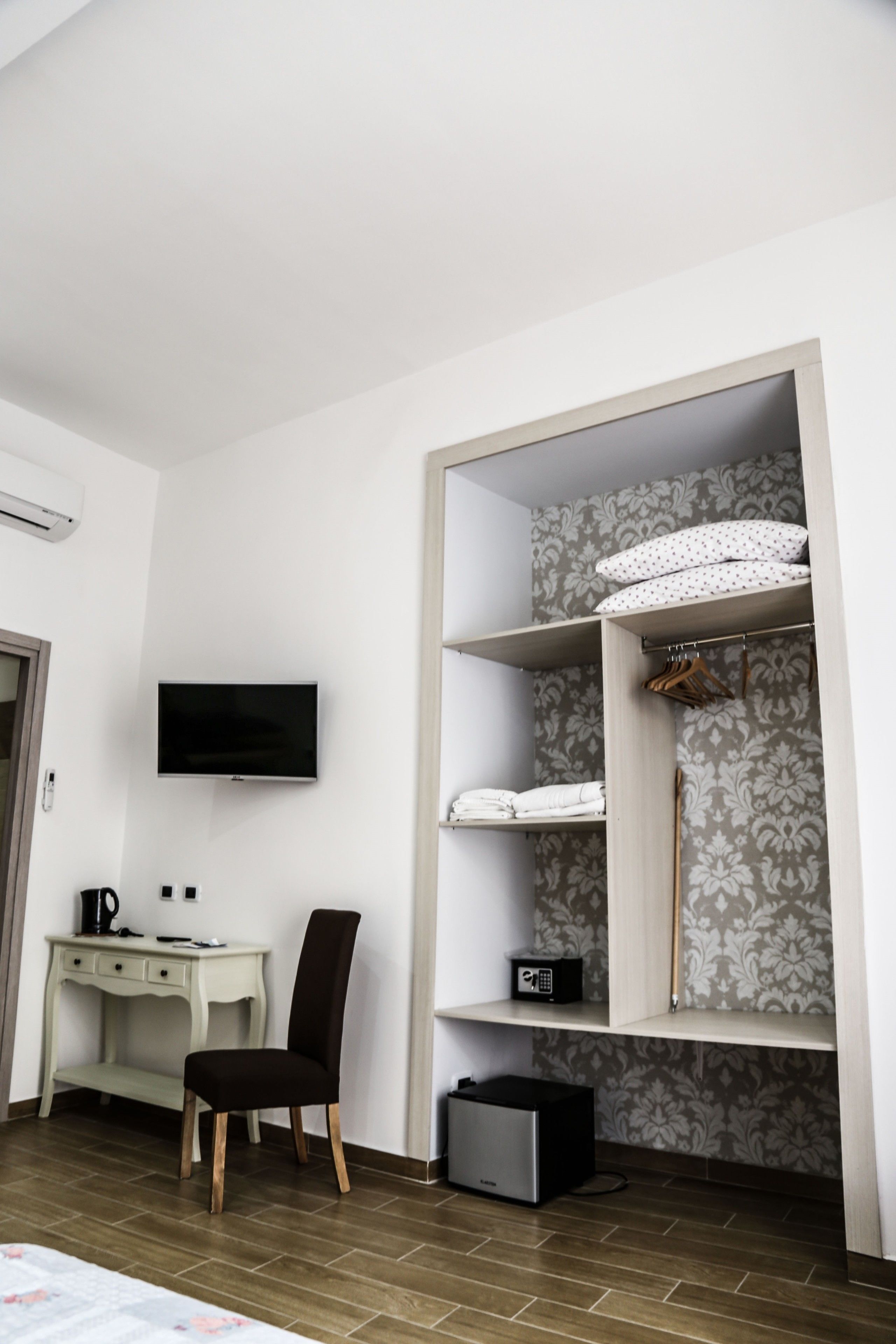 A bedroom with a bed, a desk with a chair, a TV, a wardrobe, and a suitcase.