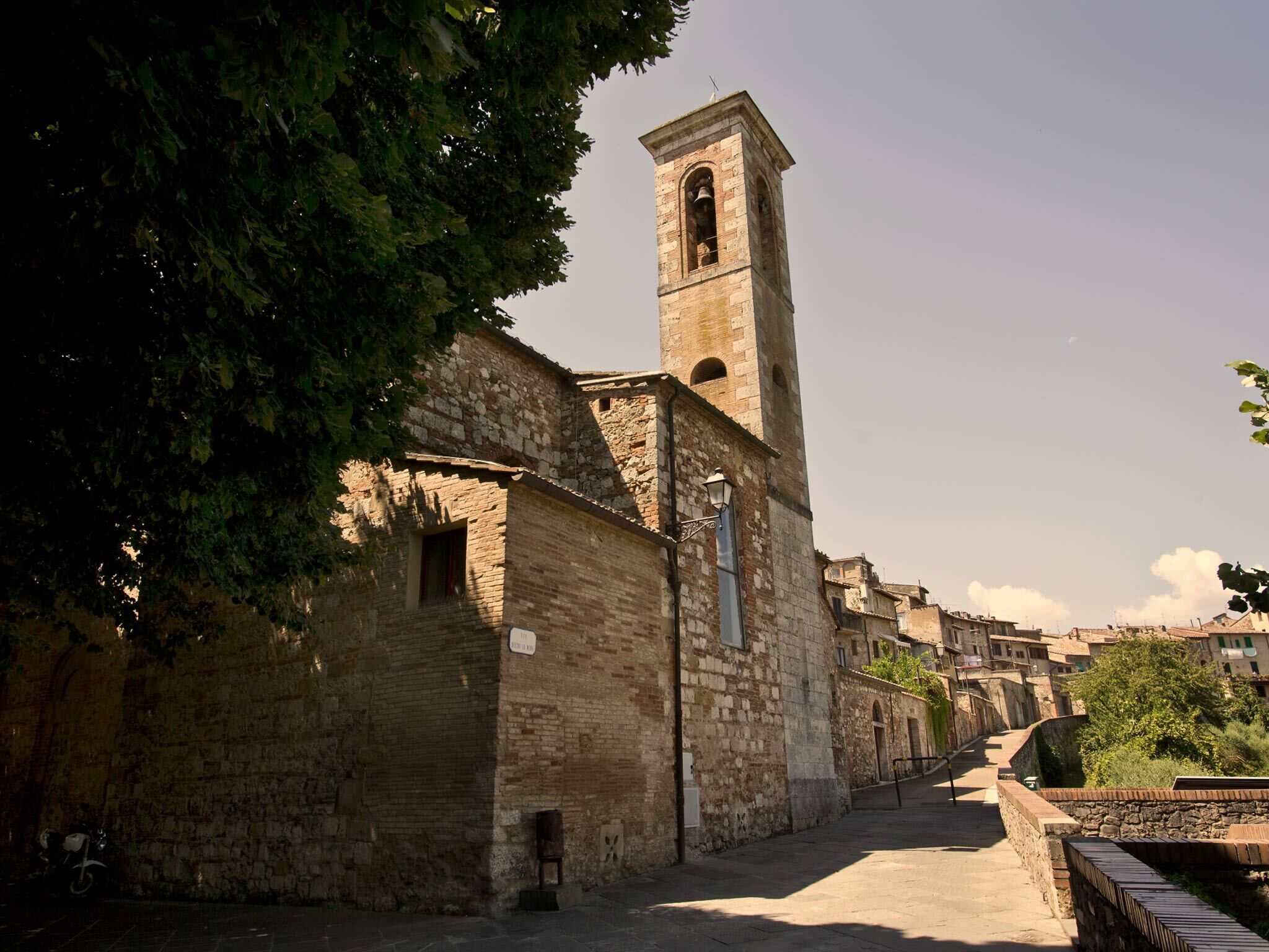 A narrow street with a historic stone building featuring a bell tower.