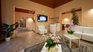 A hotel lobby with a reception desk, seating area, television, and potted plants. - Hotel Palazzo Renieri - 3stelle S (Colle di Val d'Elsa)