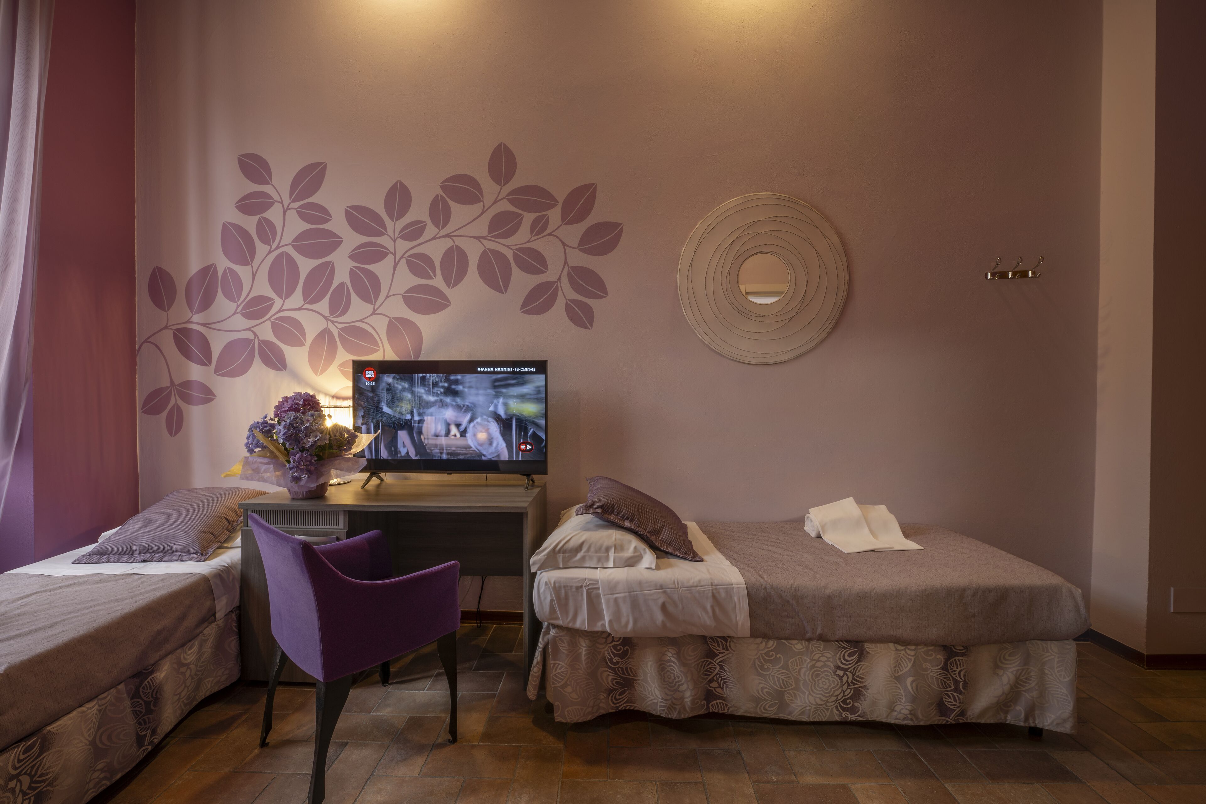 Habitación de hotel con dos camas, un escritorio con televisor, una silla y un adornado en la pared.