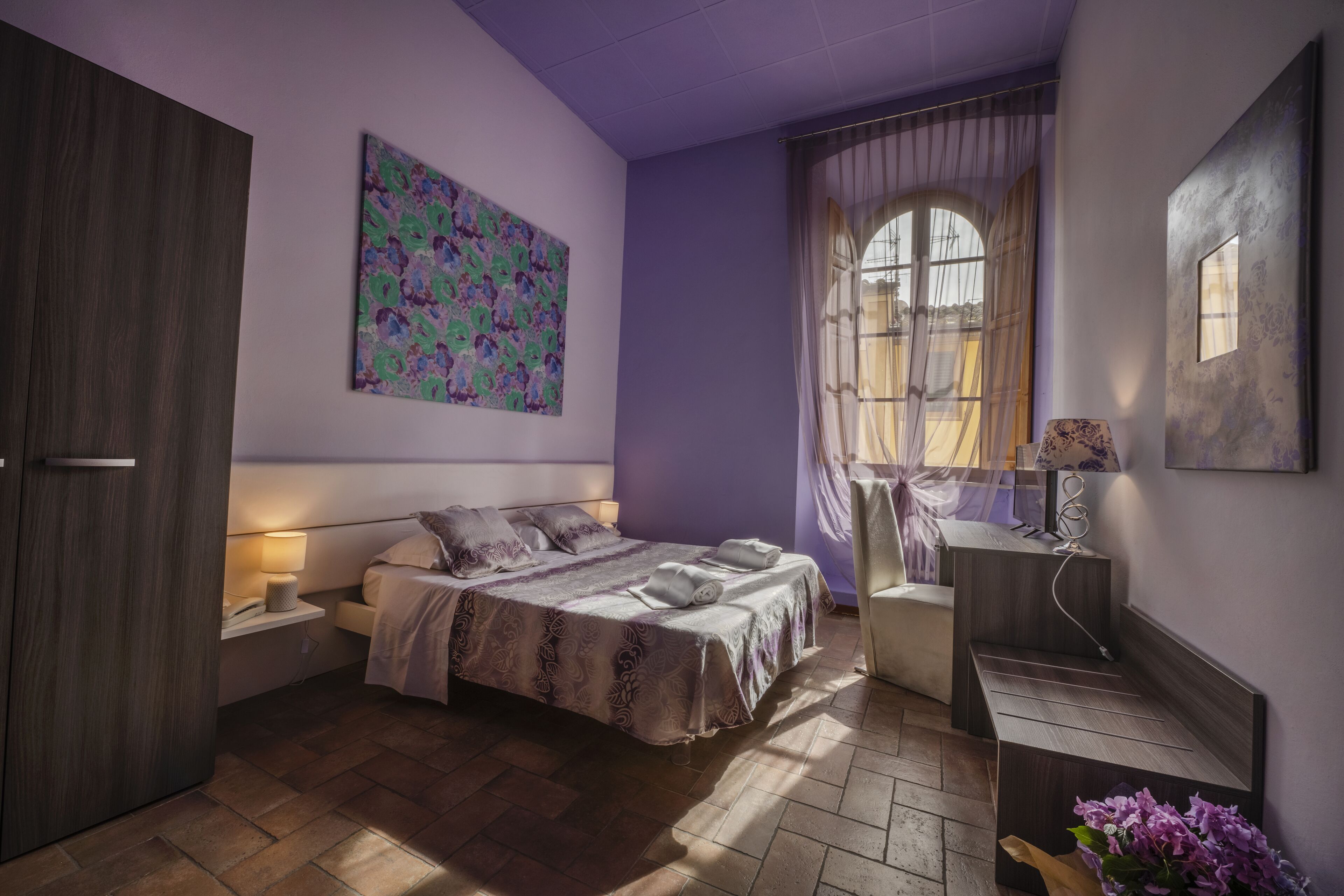 A bedroom with a bed, bedside tables, a desk, and a window with curtains.