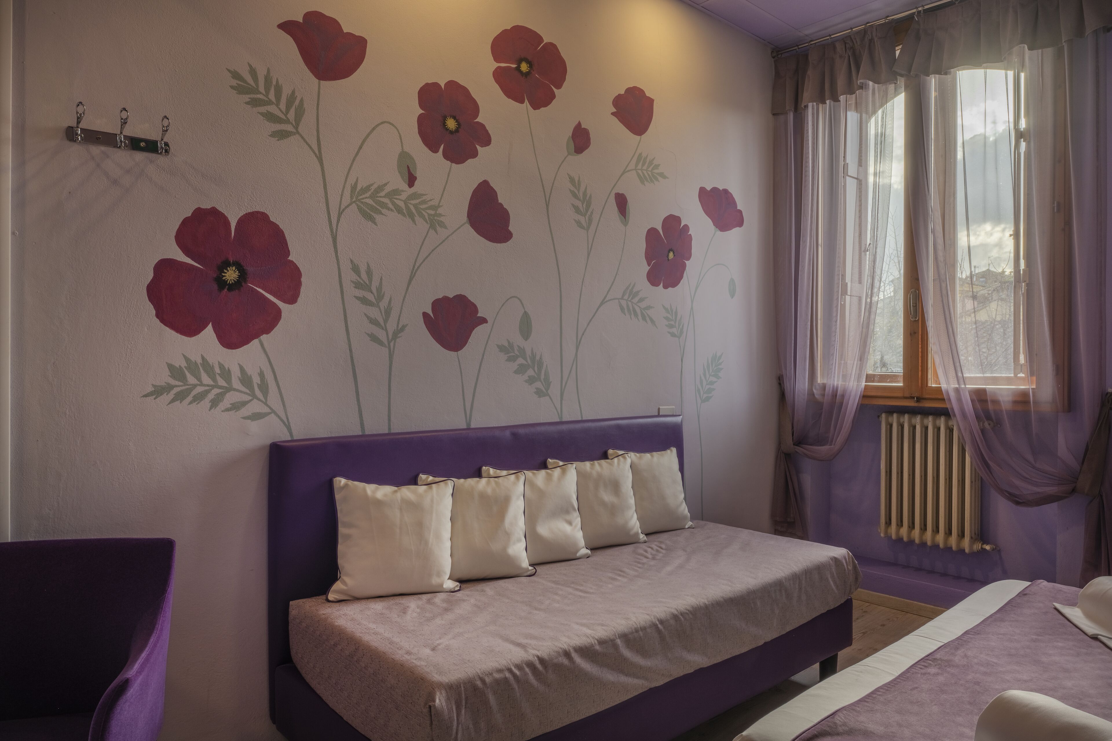 Une chambre à coucher avec une tête de lit violette, un lit avec une literie blanche et beige, et une fresque murale représentant des fleurs rouges.