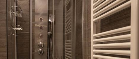 A modern shower enclosure with a glass door, a towel rack with two towels, and a built-in heater.