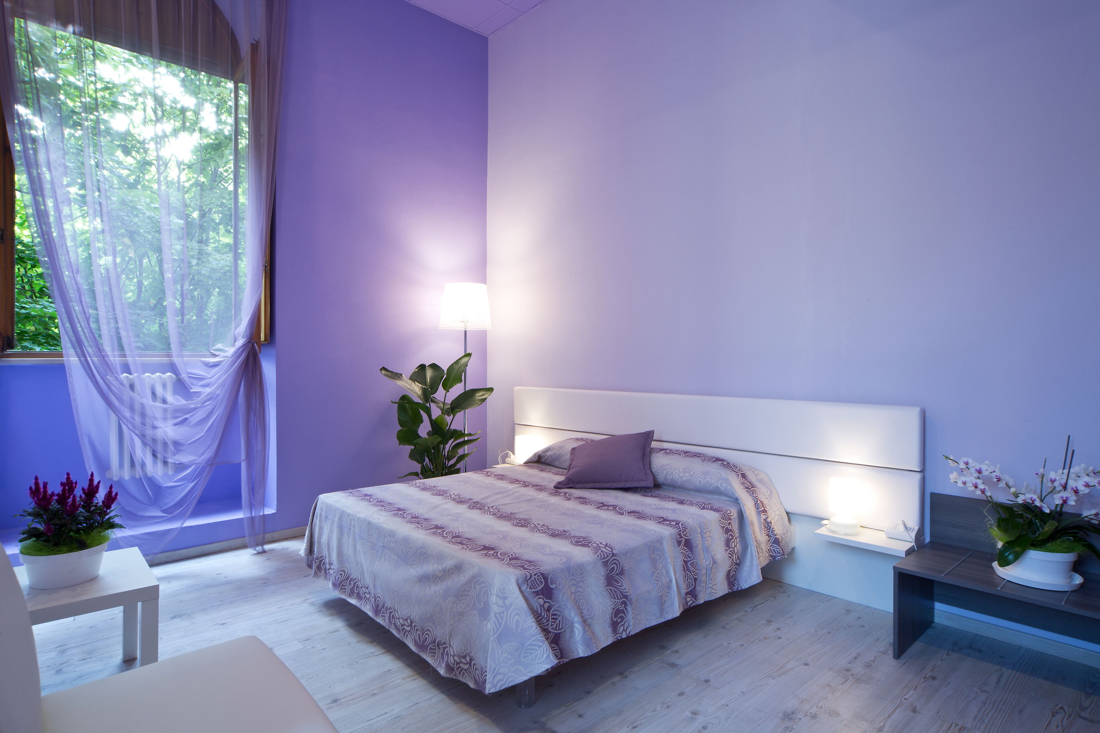 A modern bedroom with a large bed, bedside tables, and a window with sheer curtains.