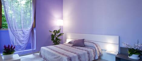 A modern bedroom with a large bed, bedside tables, and a window with sheer curtains.
