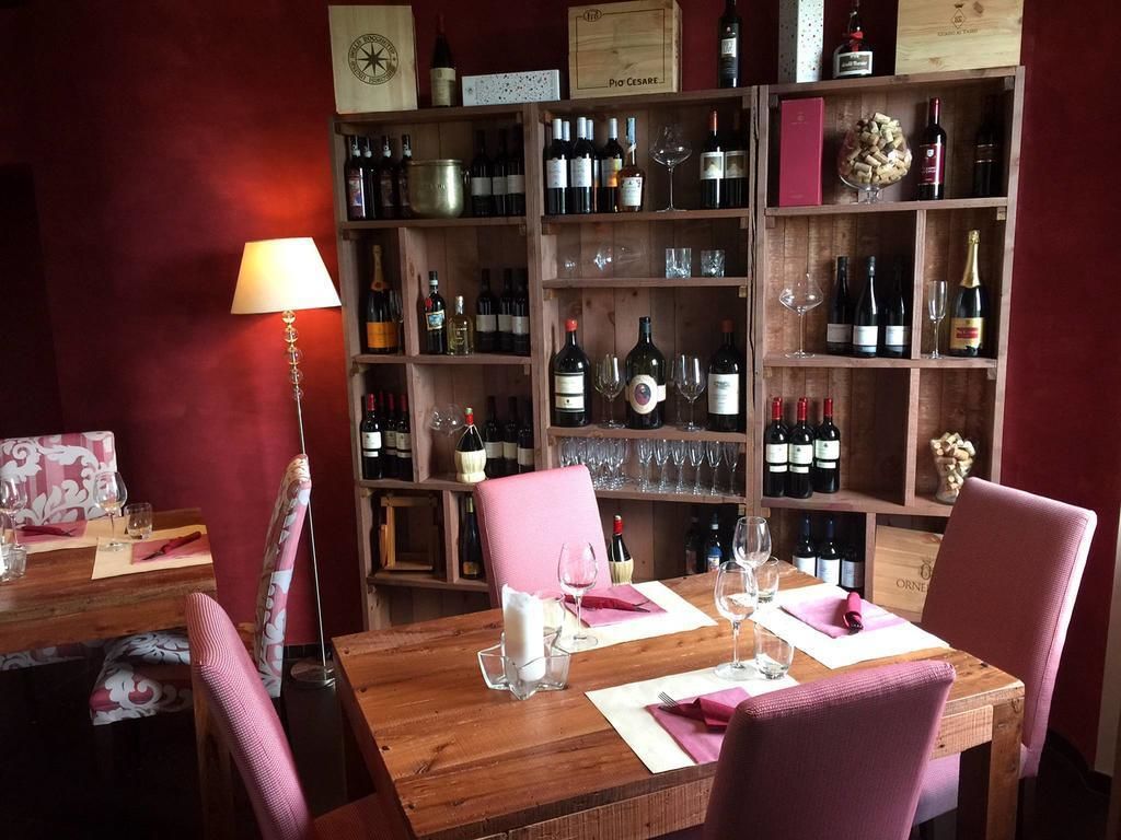 A dining area with a wooden table set for two, surrounded by wooden shelves filled with wine bottles and glasses.