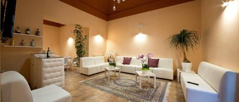 A spacious living room with a high ceiling, a chandelier, a white sofa set, a coffee table, and a large potted plant.