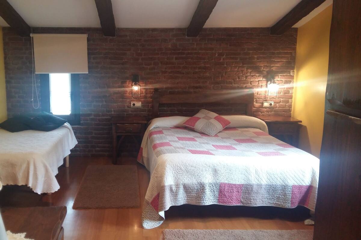 Una habitación con dos camas, una pared de ladrillo, suelo de madera y una ventana con persiana.
