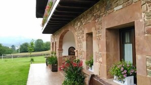 A stone building with a balcony adorned with flowers, a bench, and potted plants. - Lezamakoetxe (Sopuerta)