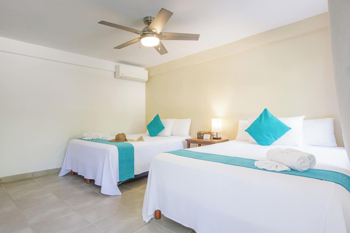 Une chambre d’hôtel avec deux lits, un ventilateur de plafond, des lampes de chevet et une petite table.