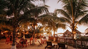 Un restaurante frente al mar con terraza, palmeras y luces colgantes.
