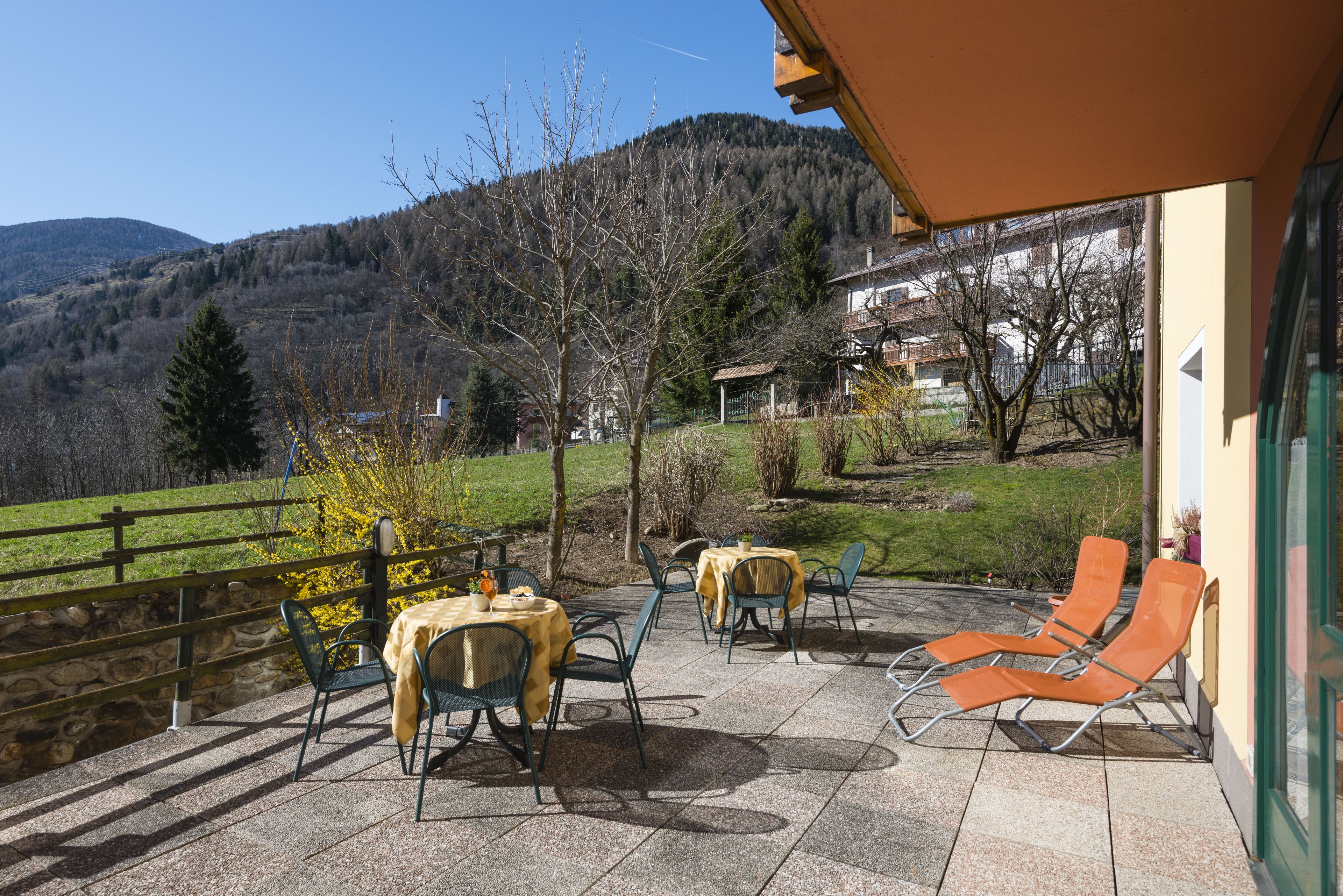 An outdoor patio with tables and chairs, a stone wall, and a view of a mountain and forest.
