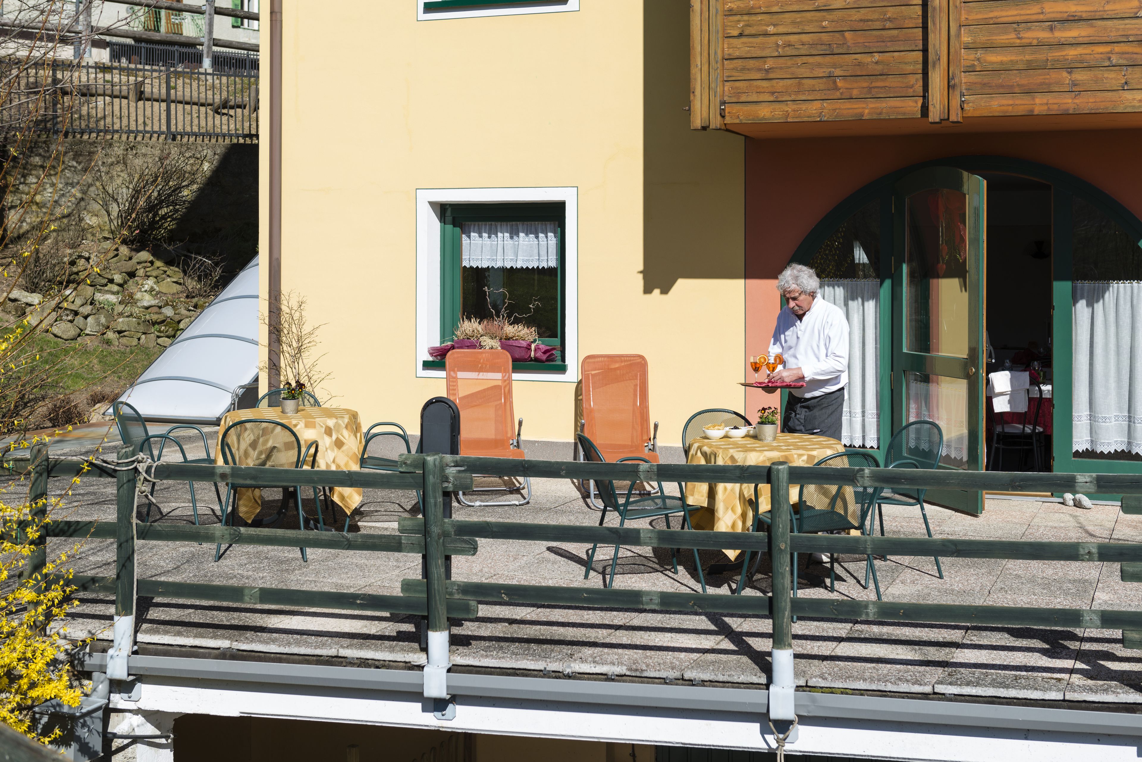 An outdoor seating area with tables and chairs, a wooden fence, and a building with a window and door.