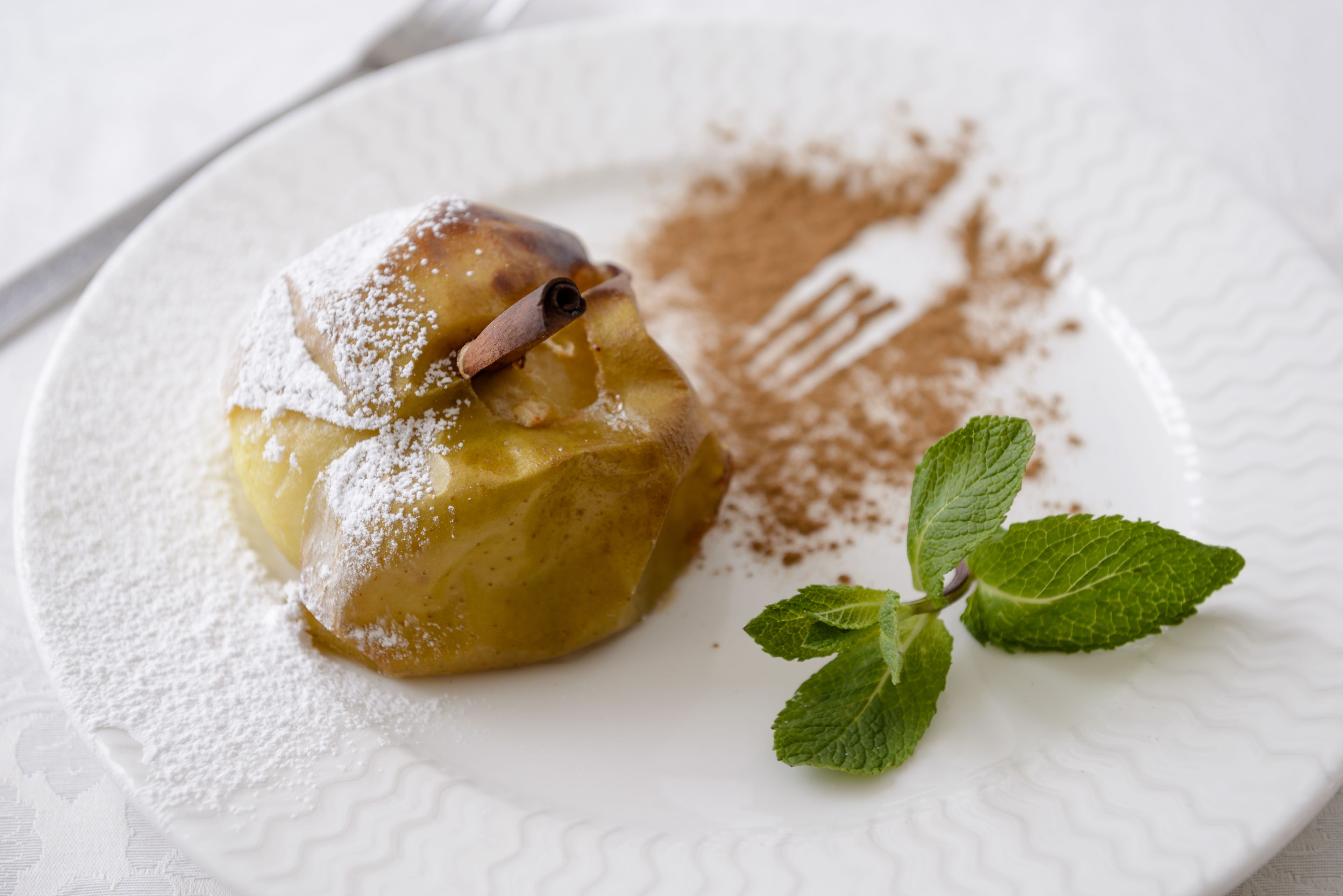 Un postre en un plato con azúcar glas y una hoja de menta.
