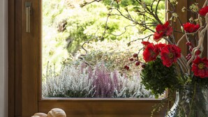 Una mesa de desayuno con pasteles, frutas y un florero junto a una ventana con cortinas de encaje.