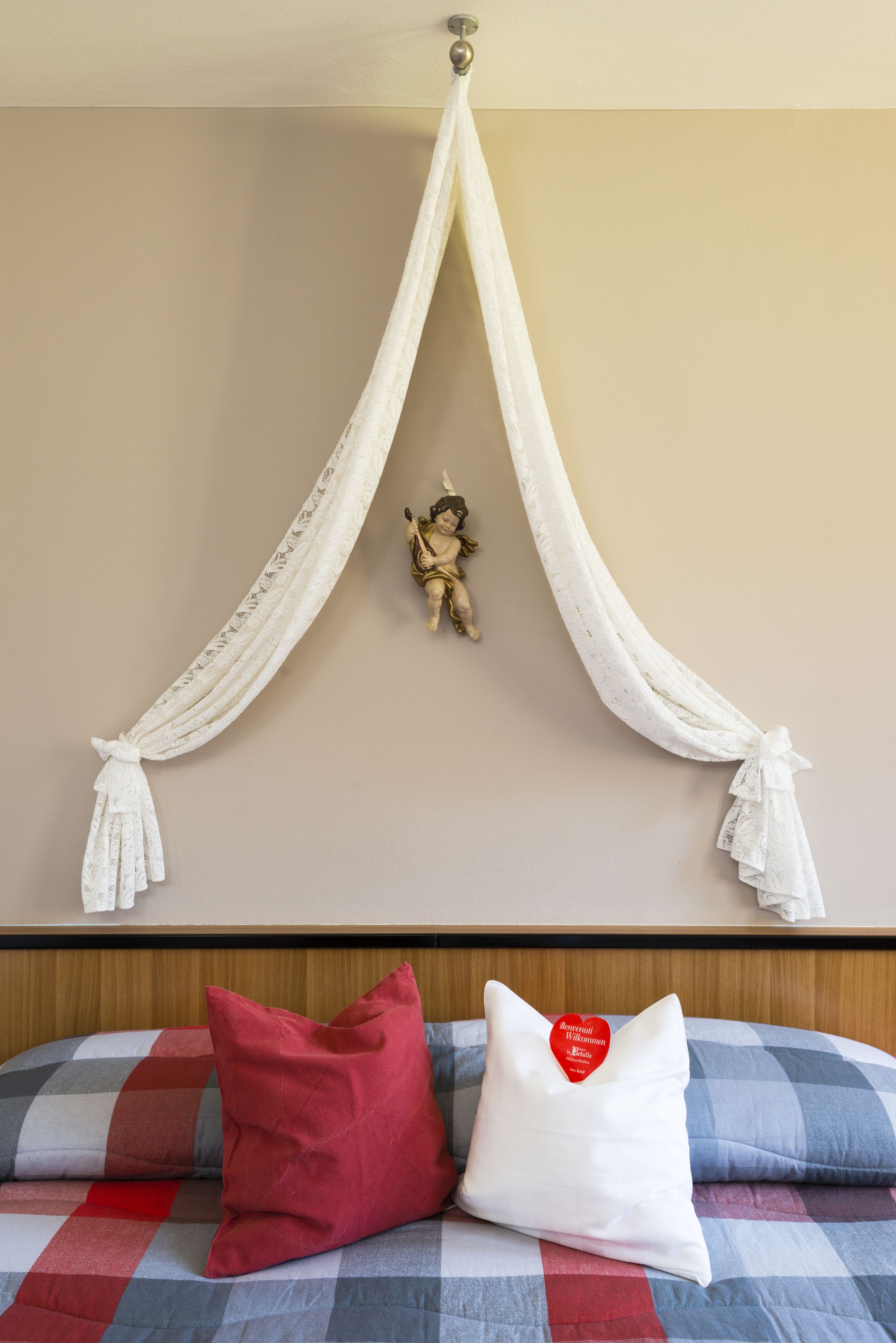 A bed with a checkered bedspread, a red pillow, and a white pillow with a heart-shaped tag.