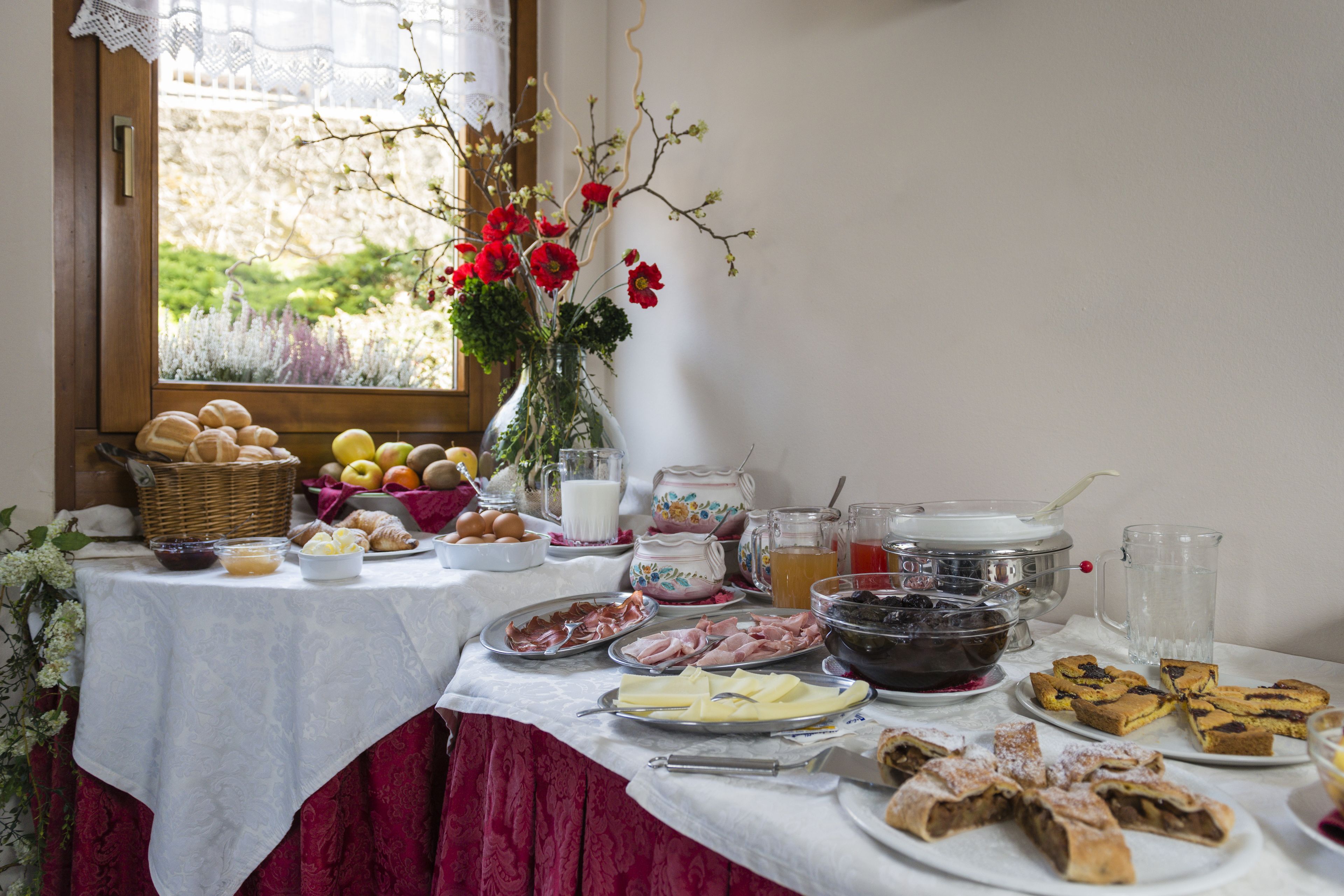Une table de petit-déjeuner avec divers aliments, un vase rempli de fleurs et une fenêtre donnant sur un paysage verdoyant.