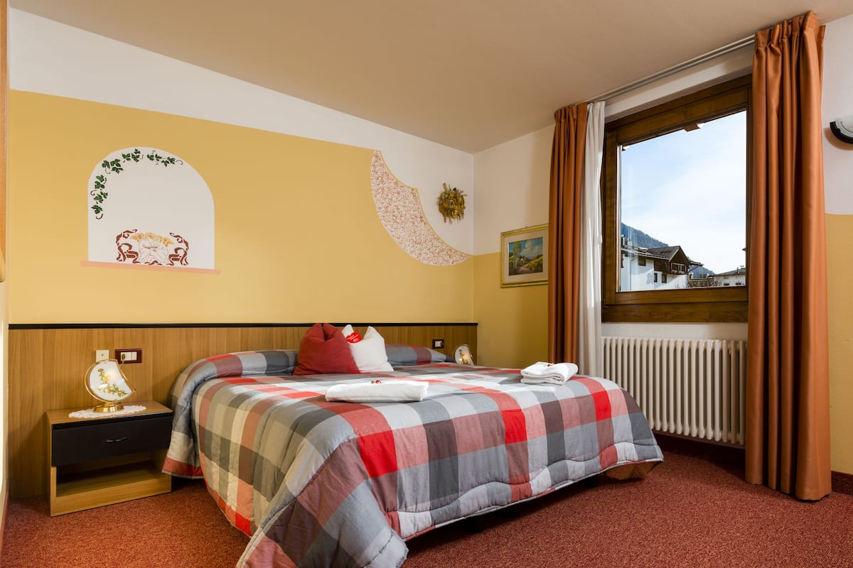 A hotel room with a bed, a nightstand, a window with curtains, and a wall with a decorative arch and a picture.