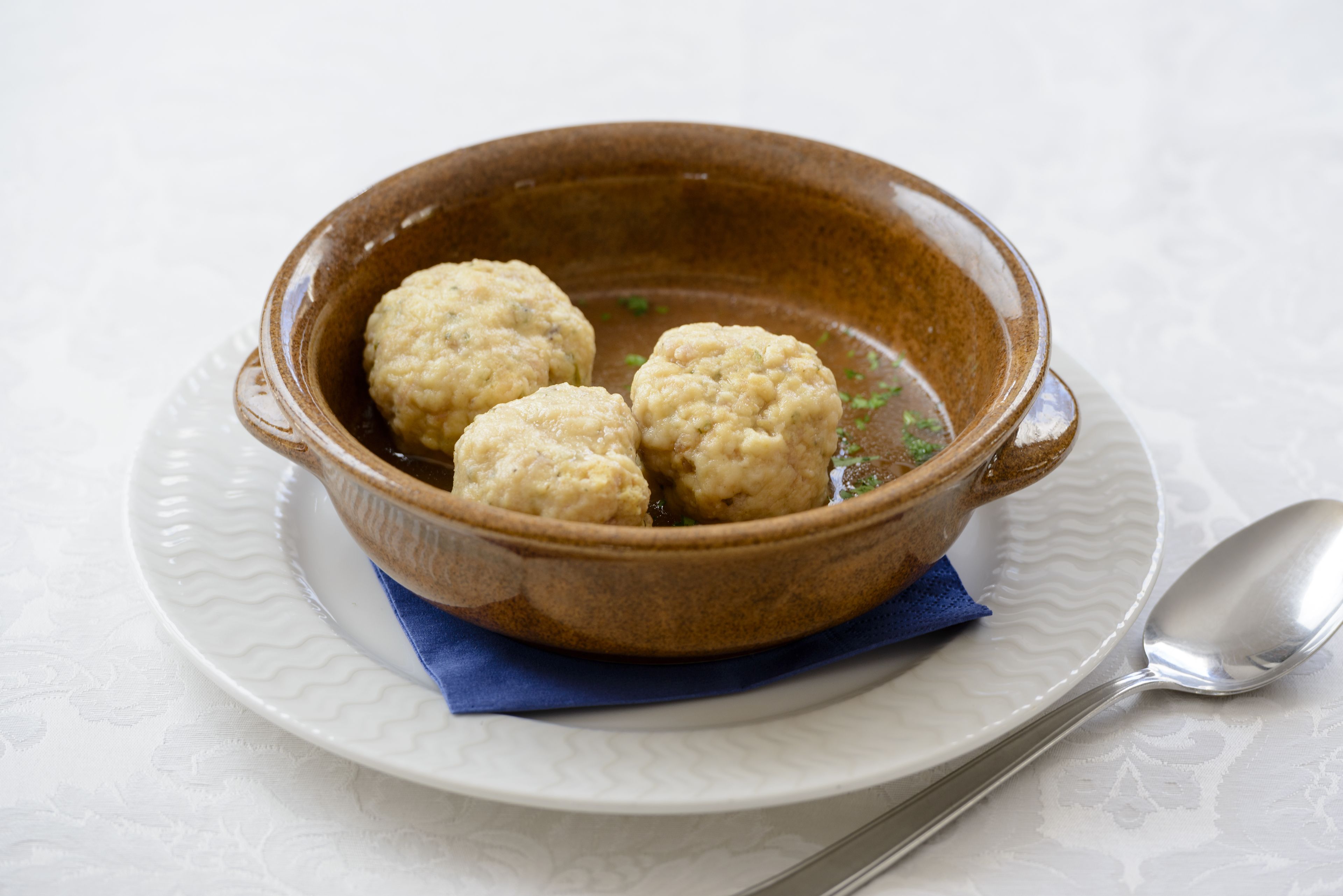 A bowl of three dumplings on a white plate with a spoon.