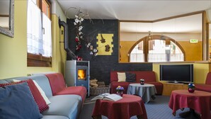 Una habitación acogedora con un sofá, dos mesitas con mantel rojo de lunares, un televisor y una chimenea.