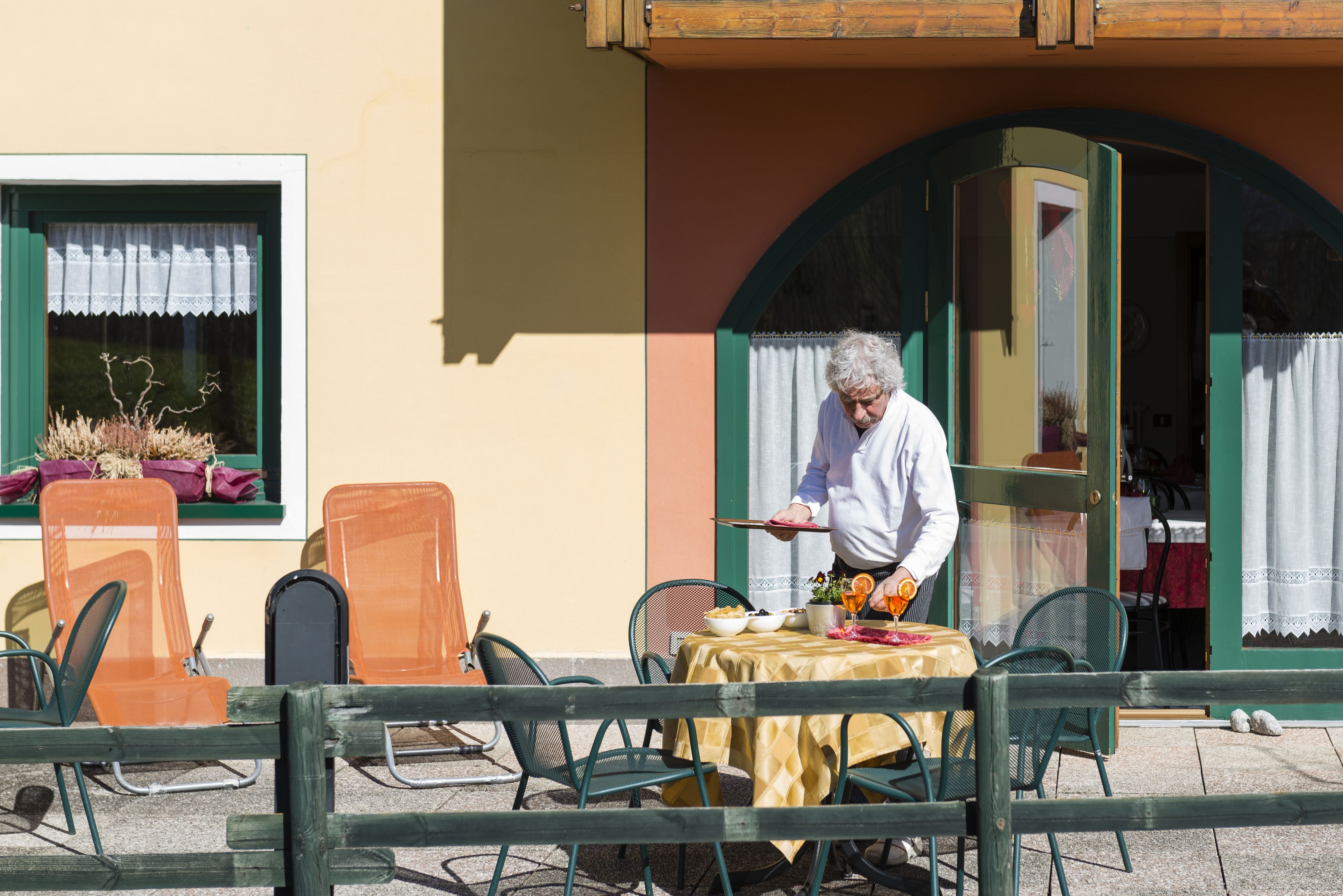 A table set outdoors with a tablecloth, chairs, and a person standing by the table.