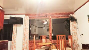 Un comedor con mobiliario de madera, un ventilador de techo y un puerta corrediza de vidrio que da a otra habitación.