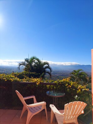 A patio with two white plastic chairs and a small table, overlooking a scenic view of a city and mountains under a clear blue sky. - Loma Tranquila (San Isidro)