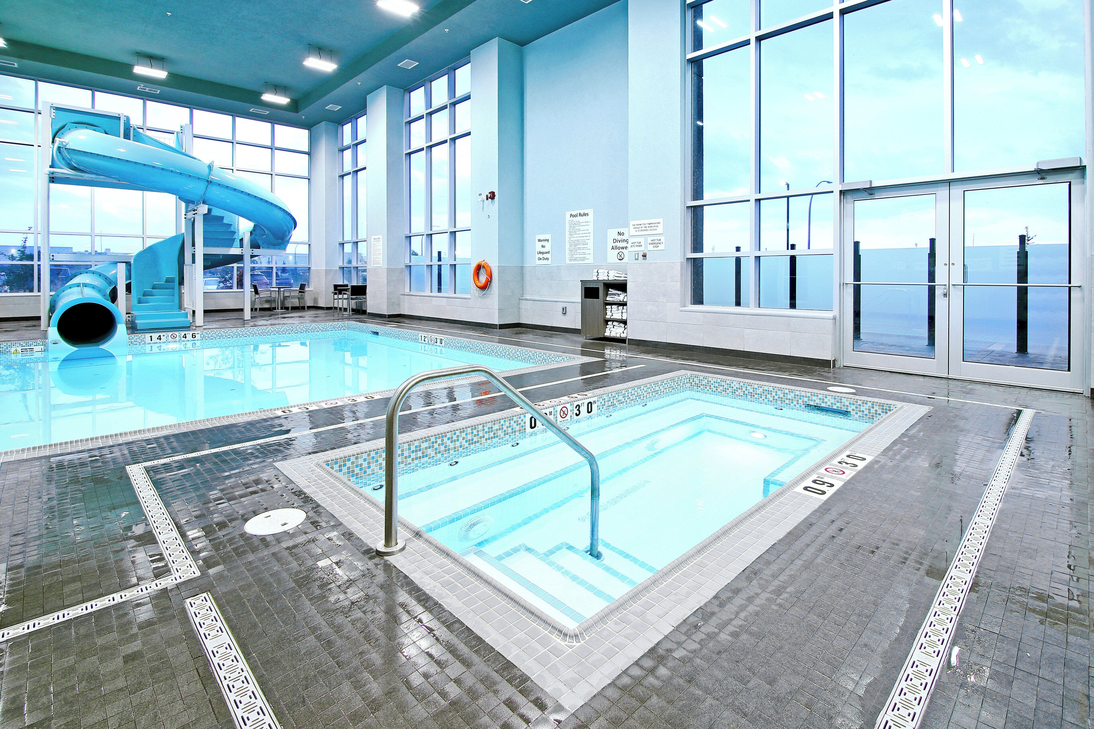 Una piscina interior con un tobogán azul, zona de piscina despejada y grandes ventanales.