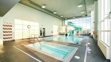 Una piscina interior con tobogán, marcas claras en la piscina y un reloj en la pared.