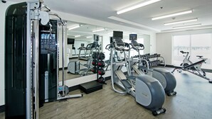 Un gimnasio con máquinas de cardio, equipo de levantamiento de pesas y un espejo grande.