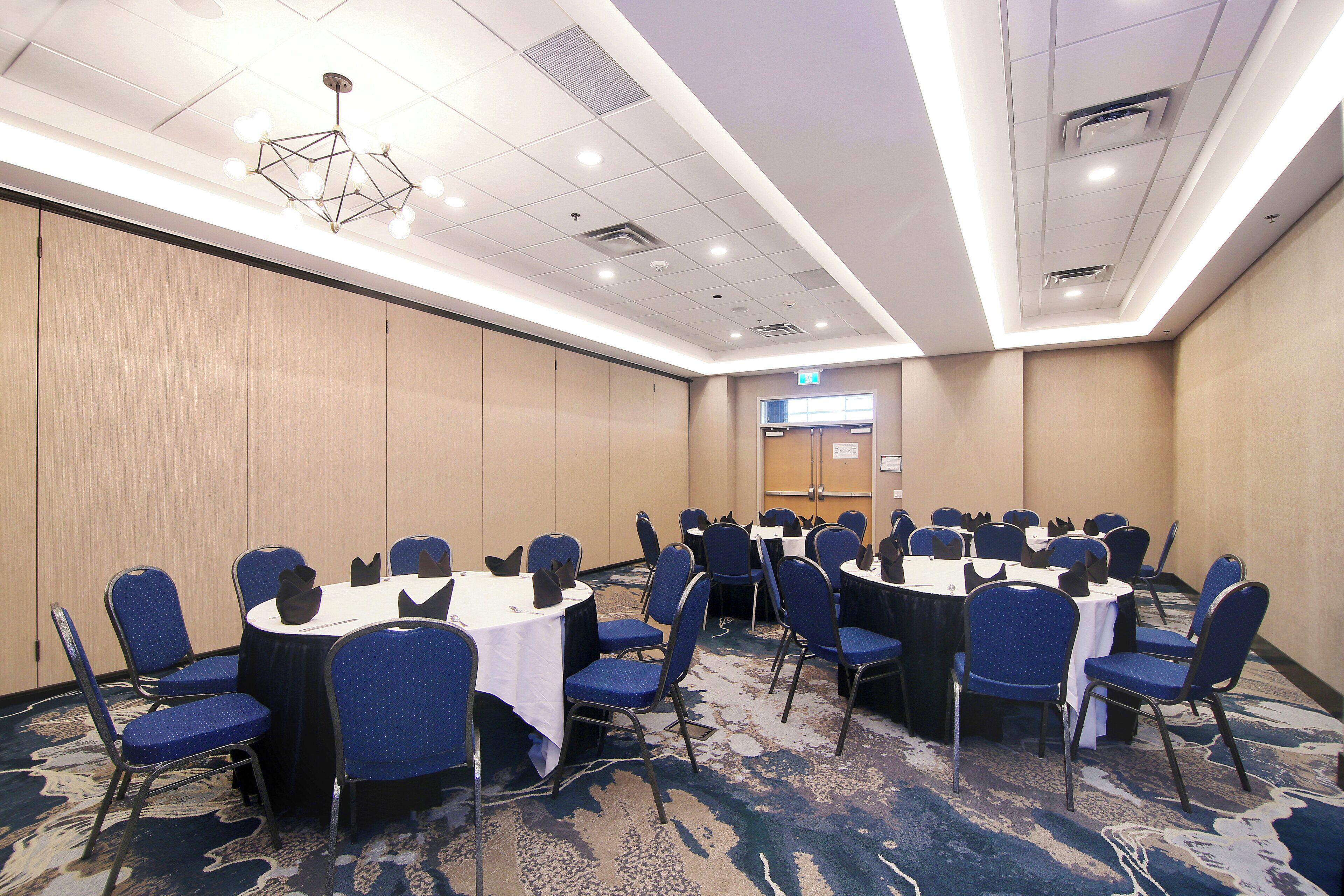 Un salón de conferencias con mesas redondas, sillas azules y una alfombra estampada.