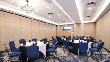 Un salón de conferencias con mesas redondas, sillas azules y una alfombra estampada.