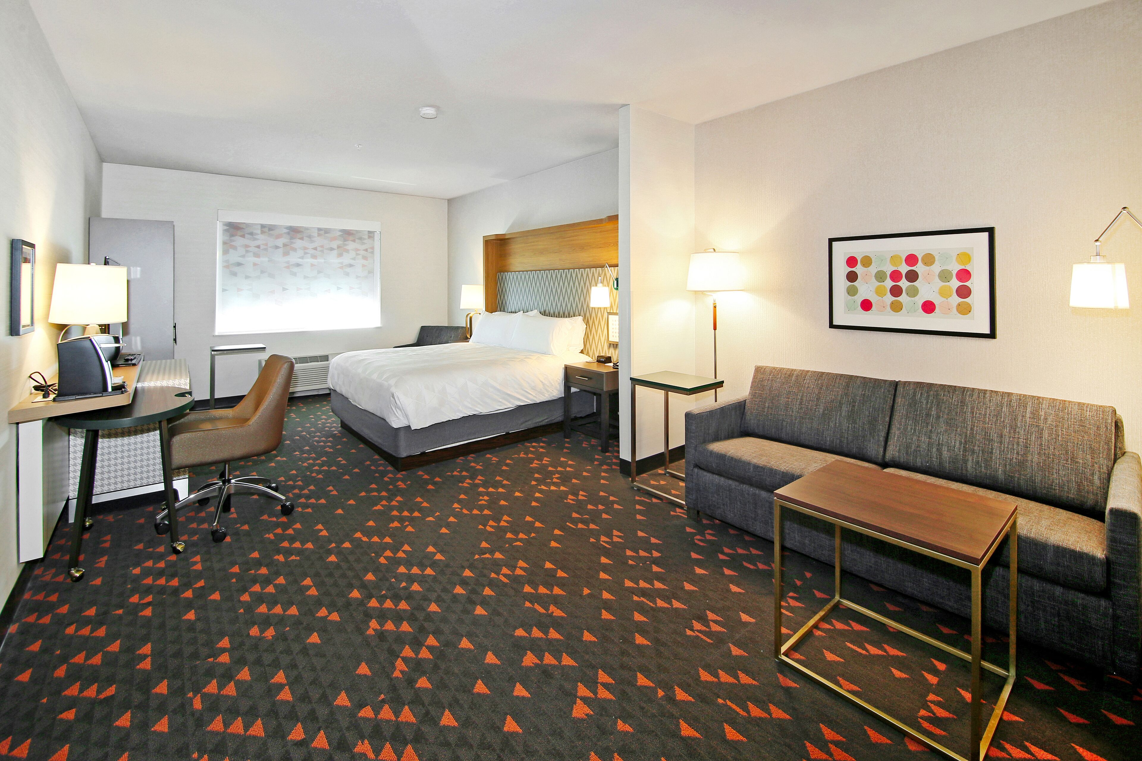 A hotel room with a bed, a desk with a chair, a sofa, and a small table.