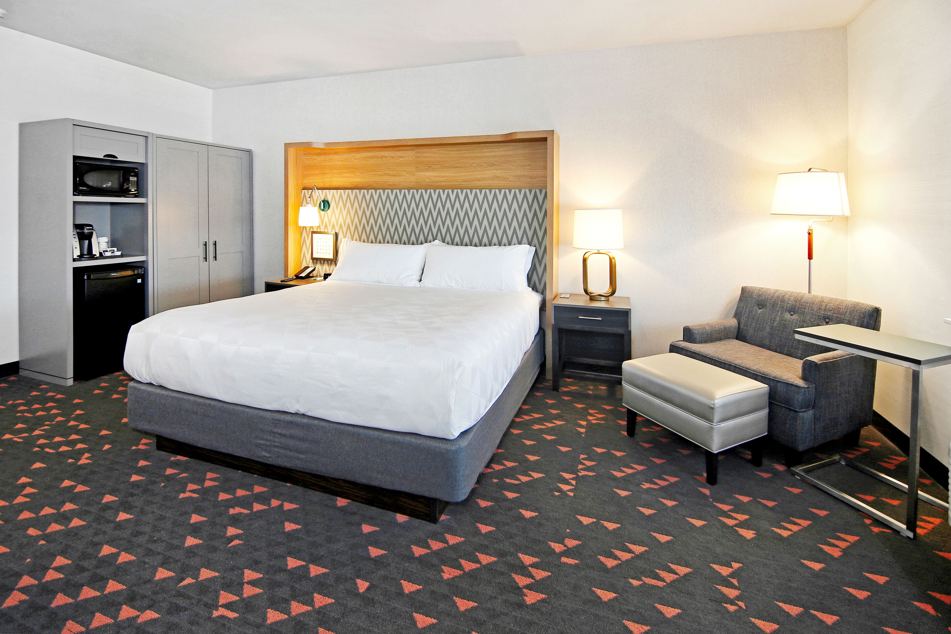 A hotel room with a large bed, a desk, a chair, a wardrobe, and a microwave.