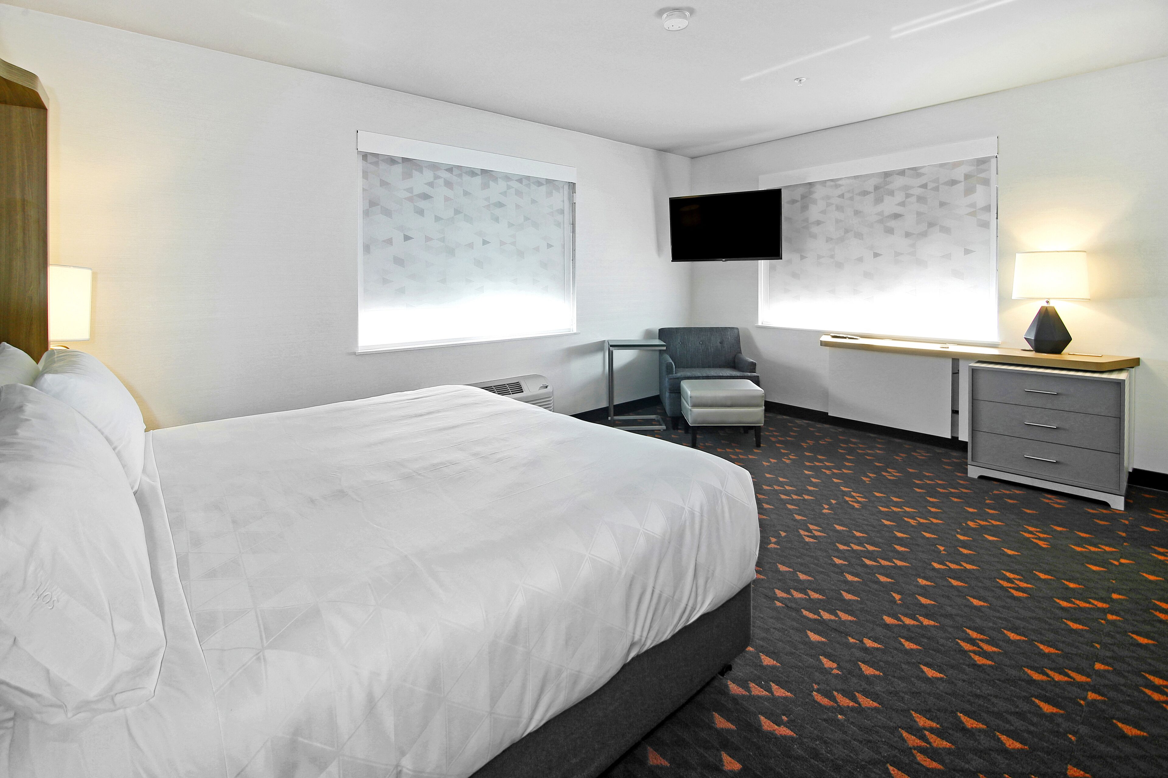 Une chambre d’hôtel avec un grand lit, un bureau, une chaise, une télévision et une commode.