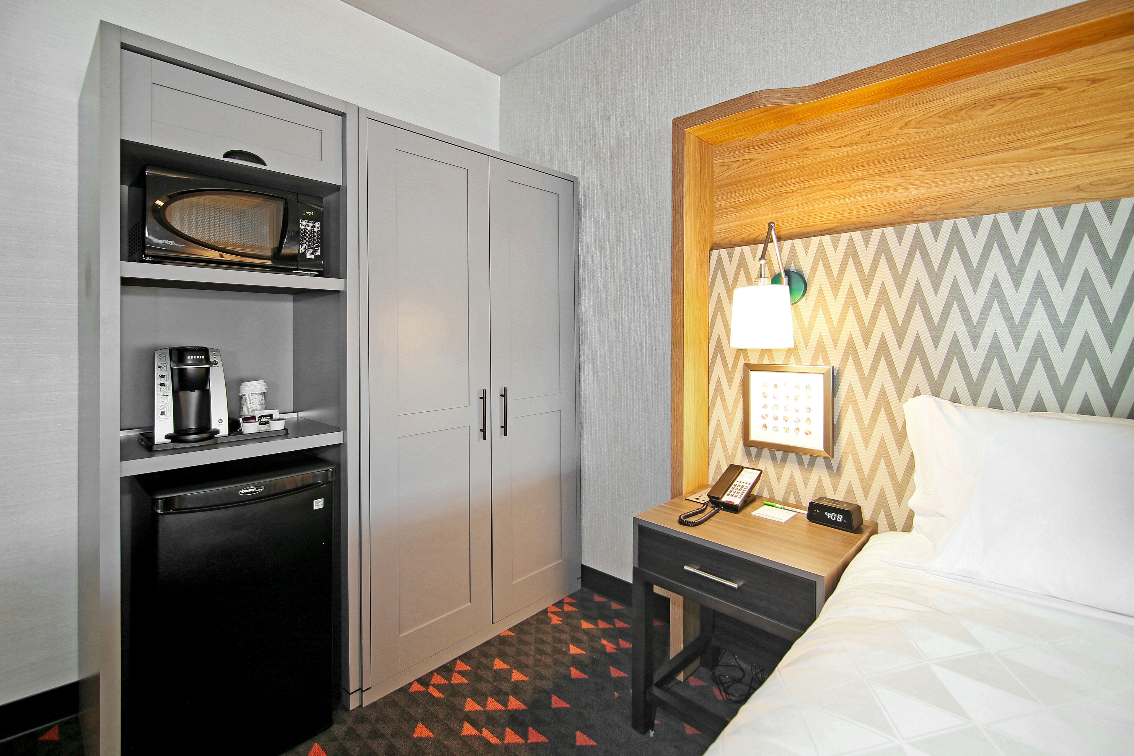 A hotel room with a bed, a desk with a phone, a microwave, and a mini-fridge.
