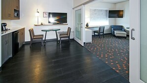 Una cocina moderna con piso de madera oscura, un comedor con mesa y sillas, y una sala de estar con sofá y televisor.