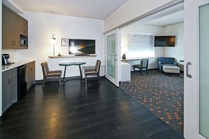 A modern kitchen with dark wood flooring, a dining area with a table and chairs, and a living area with a sofa and TV. - Holiday Inn Hotel & Suites Calgary Airport North by IHG (Calgary)