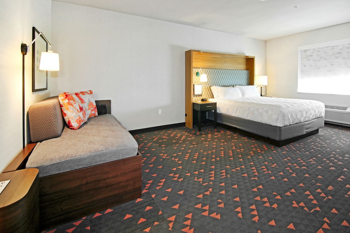 A hotel room with a sofa, a bed, a nightstand, and a wall-mounted lamp.