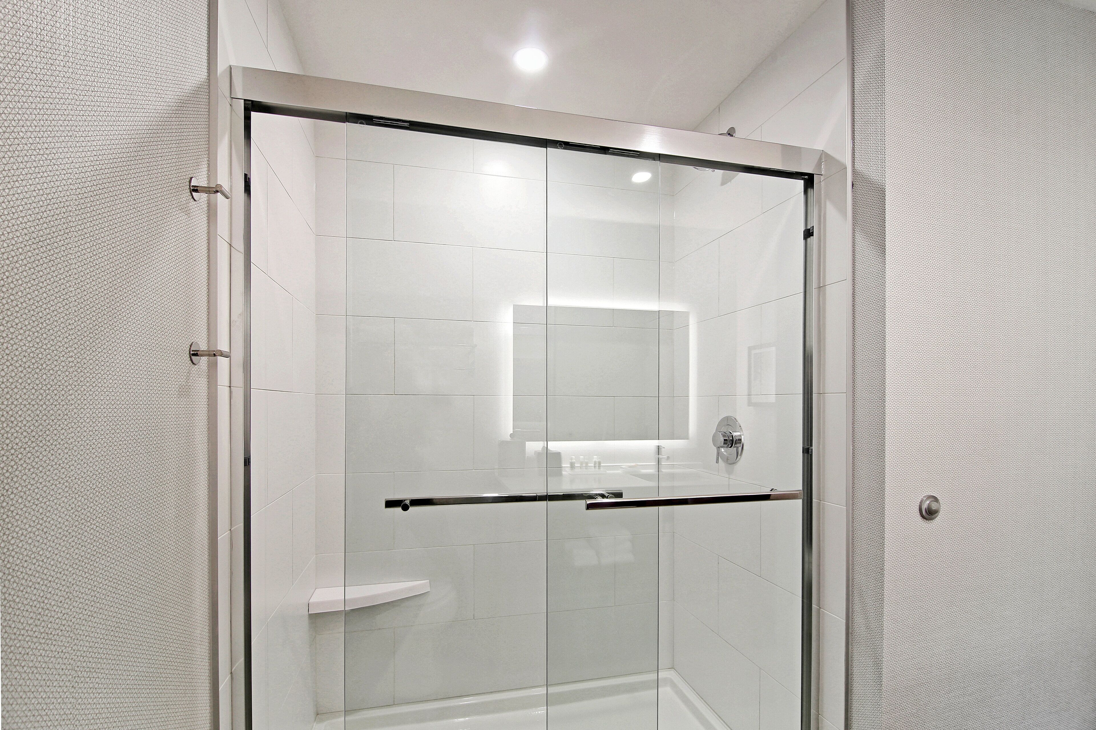 A modern shower with a glass door, white tiled walls, and a visible shower control panel.