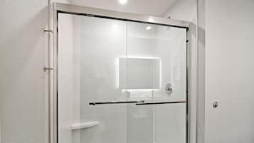 A modern shower with a glass door, white tiled walls, and a visible shower control panel.
