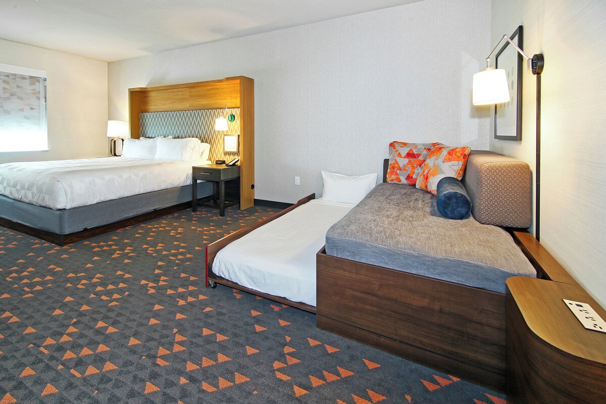 A hotel room with two beds, a desk, a chair, and a lamp.