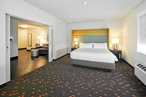 A hotel room with a large bed, a bedside table with a lamp, a chair, and a small table. There is a hallway leading to another room. - Holiday Inn Hotel & Suites Calgary Airport North by IHG (Calgary)