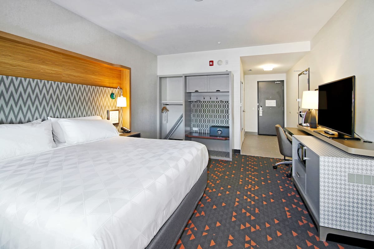 A hotel room with a bed, desk, TV, and closet.