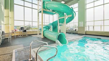 Una piscina interior con un tobogán de agua verde, zona de piscina despejada y amplias ventanas.