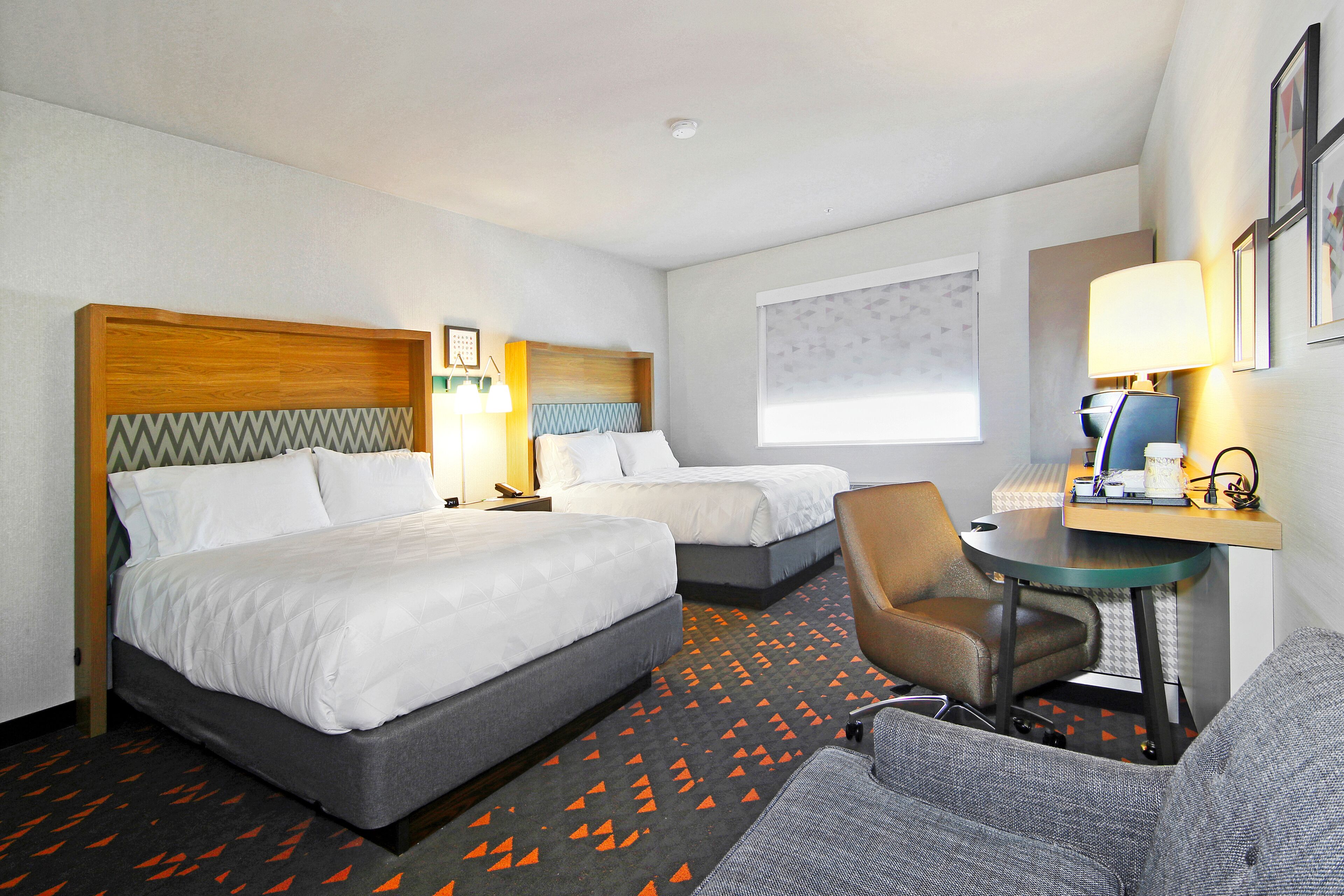 A hotel room with two beds, a desk, a chair, and a small table.