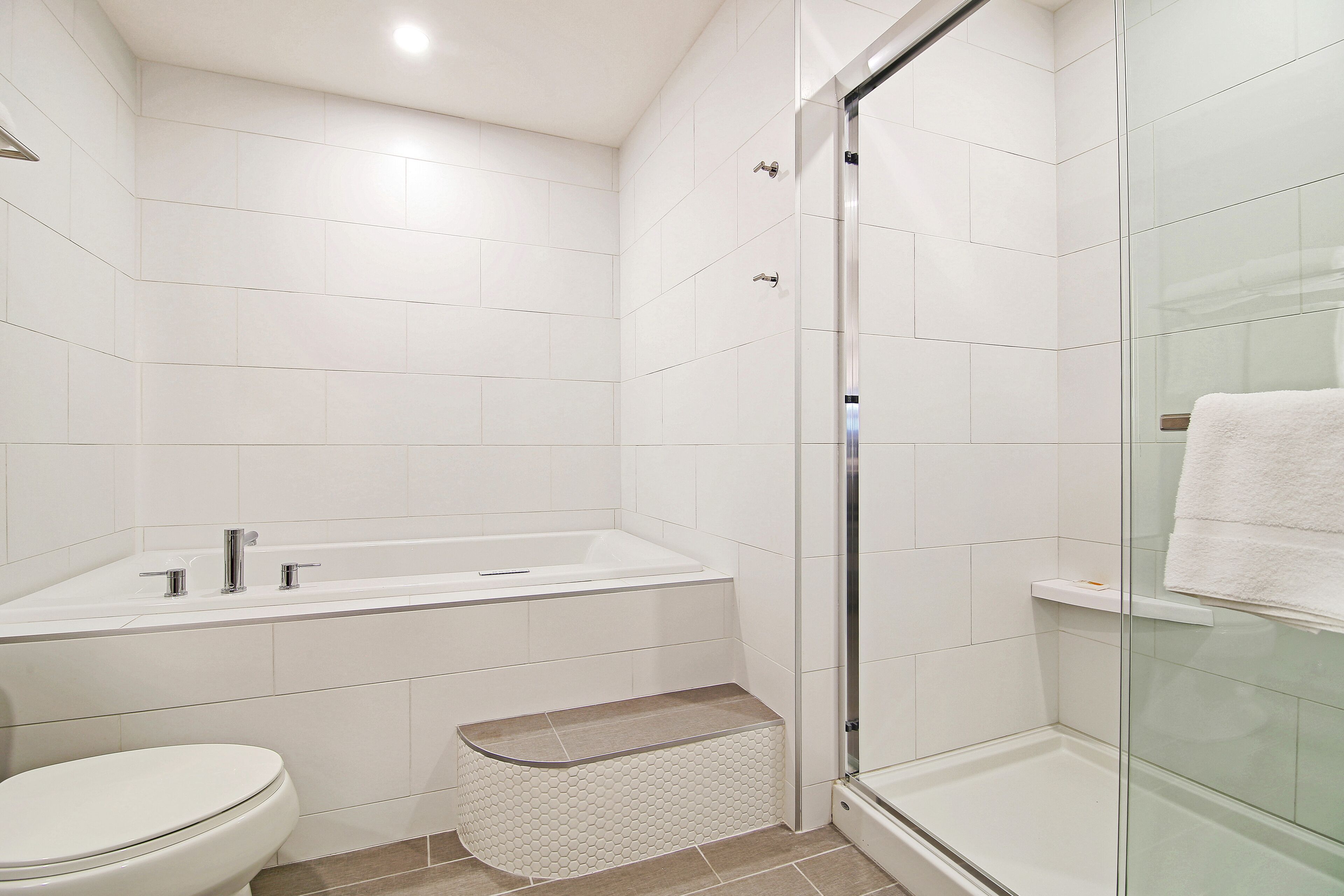A modern bathroom with a white toilet, a bathtub, and a glass shower enclosure.