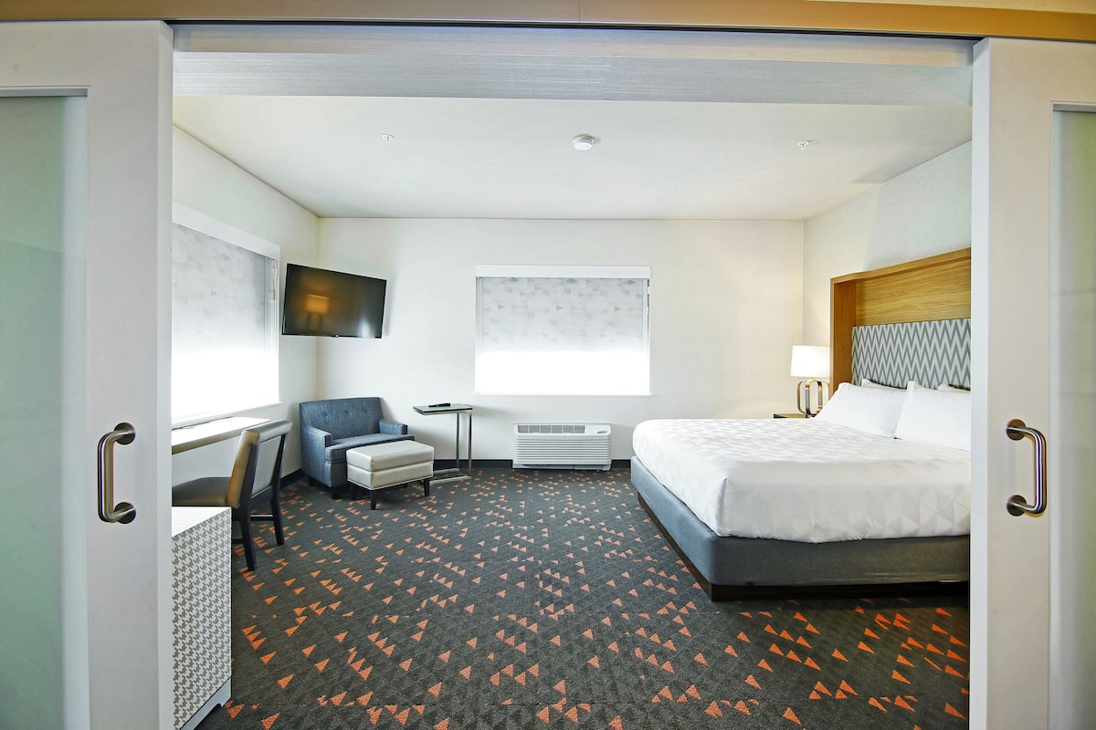 A hotel room with a bed, a desk, a chair, a TV, and a window.