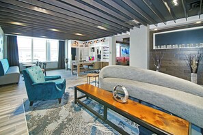 Una sala moderna con un sofá, un sillón azul, una mesa de centro de madera y un comedor con una mesa y sillas.