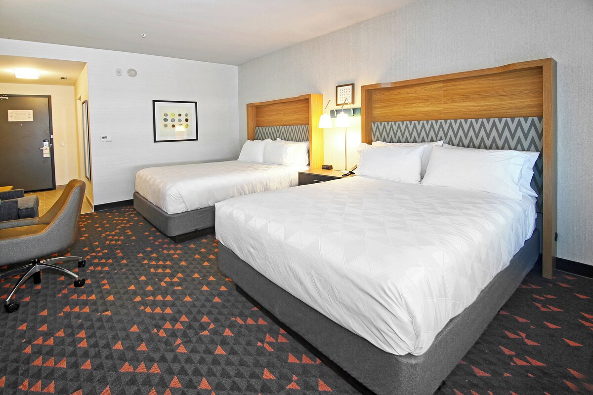 A hotel room with two beds, a desk, and a chair.